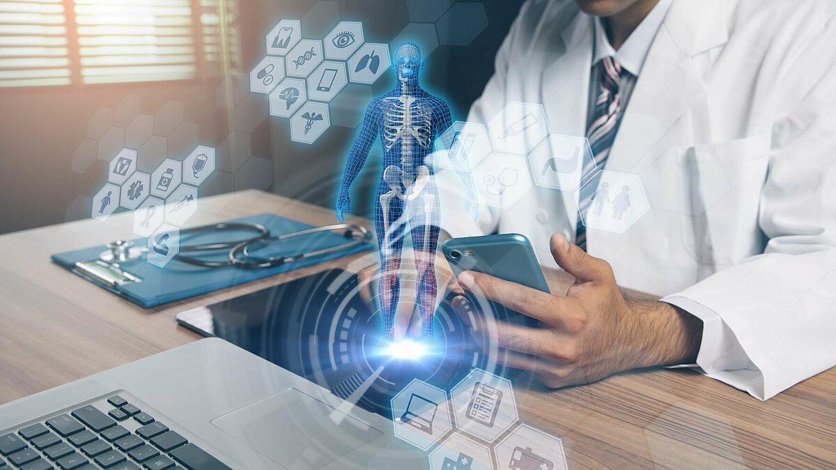 Ein Arzt sitzt am Laptop. Um ihn herum sind virtuelle Icons eines Mediziniers zu sehen.